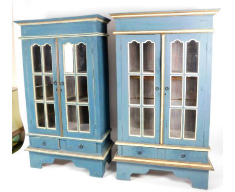 A pair of painted floor standing cabinets, each in turquoise and cream, with a shaped cornice, arched glazed doors and ring h