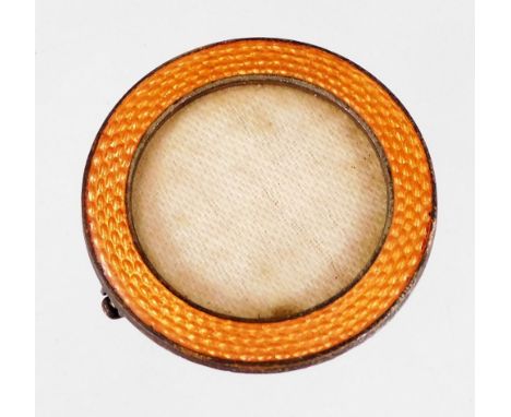 A small circular photograph frame, with orange enamel border, in silver plated frame, with a splay pin back, 3cm diameter.