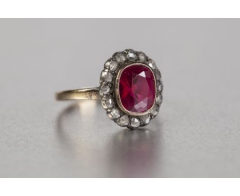 A LATE VICTORIAN/EDWARDIAN 18ct GOLD RING, set with a ruby coloured stone within a surround of tiny rough cut diamonds 