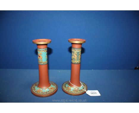 A Pair of red clay candlesticks decorated with coloured enamel bands
