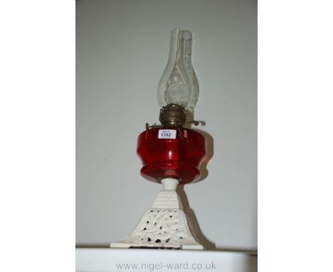 An Oil Lamp on white cast iron base with red glass reservoir.