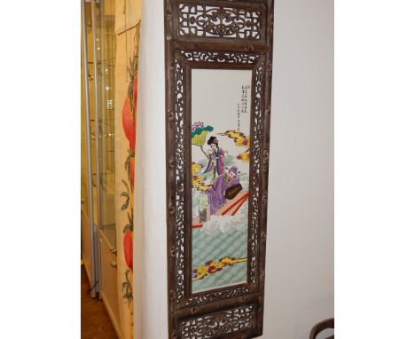 A Chinese famille rose ceramic panel, depicting figures in a garden, within a hardwood frame with pierced panels. H. 121cm