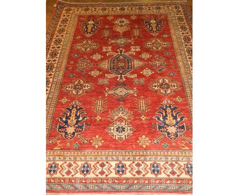 A red ground Kazak carpet, having many geometric medallions to centre, within stylised floral borders, fringed. L: 240cm W: 1