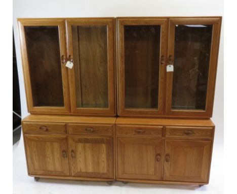 Two Ercol light elm cabinets each having top with pair of glazed doors enclosing glass shelves, the bases with drawers and cu