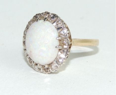 A 9 carat gold opal and diamond cluster ring, the oval shallow cabochon enclosed by eight small single cuts, finger size L1/2