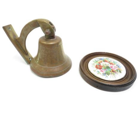 A ceramic pot lid painted with flowers mounted in circular wood frame, lid 10cm diameter together with a small brass bell and