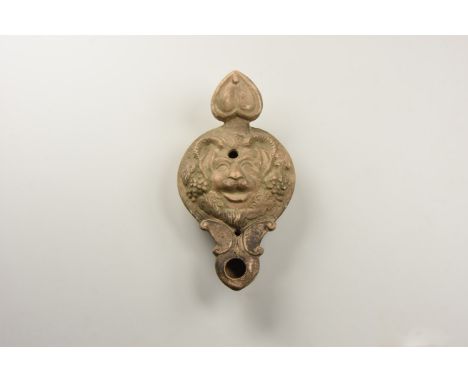 An undated archaistic cream ceramic oil lamp with lion mask to the discus framed by grapes and vineleaves, nozzle with scroll