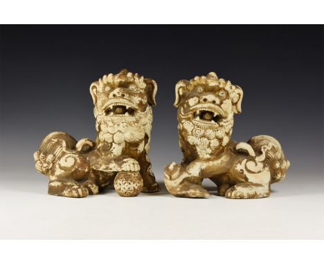 An undated archaistic opposed pair of ceramic lions each with a forepaw resting on fish or pearl, open mouth with free-runnin