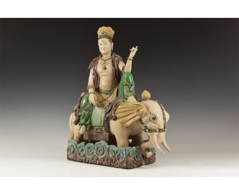 20th century AD. A polychrome glazed ceramic figure of Buddha seated on the back of an elephant, scrolled panels to the base.