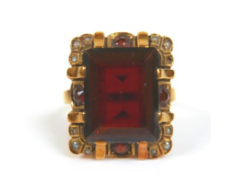 An 18ct yellow gold dress ring, set with an emerald cut red stone, possibly garnet, 14.3 by 11.2 by 4.7mm, surrounded by four