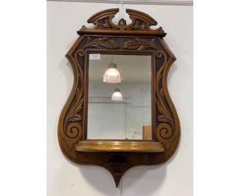 An Arts and Crafts period walnut wall hanging mirror, the frame, of Cartouche outline, carved in low relief with acanthus, an