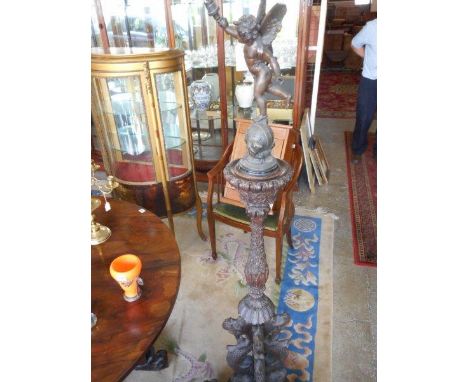 A spelter lamp in the form of Eros on a Chinese hardwood stand with carved leaf decoration to the column, on four dragon form