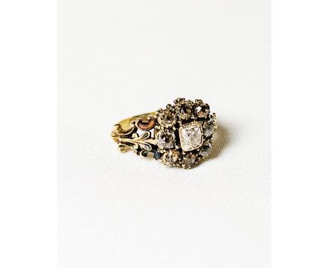 A Georgian ring set cushion shaped diamond surrounded by diamonds, on a gold shank with pierced leaf form shoulders