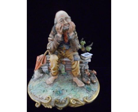 A Capodimonte figure of a tramp seated on a bench, a book and shoes to his side