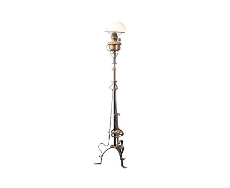 An Arts &amp; Crafts wrought iron and beaten copper standard lamp with forge wrought whiplash scrolls and brass appliques emb