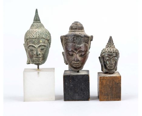 3 kleine Buddhaköpfe, Südost-Asien, 19. Jh. und früher, Bronze. 2 x auf Holz-, 1 x auf semitransparenten Acrylglassockel mont