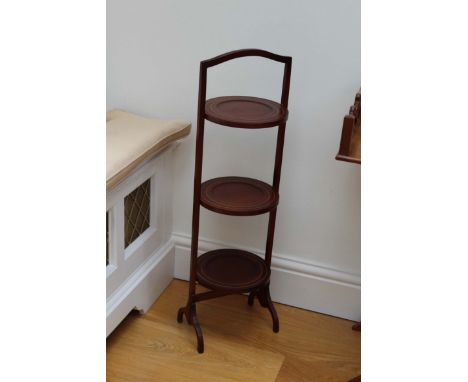A MAHOGANY THREE TIER CAKE STAND and and a cream and wicker shelf unit.

