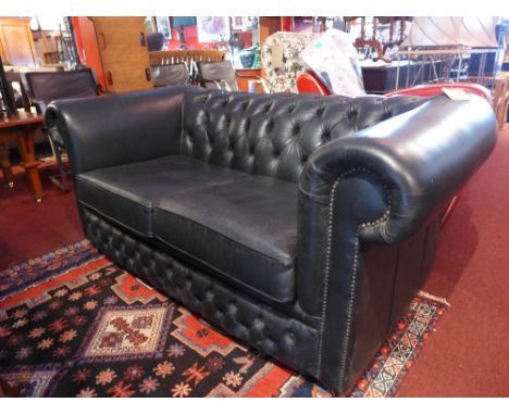 A Chesterfield style two seater sofa with black vinyl button back upholstery and raised on bun feet. H-74cm W-164cm D-85cm