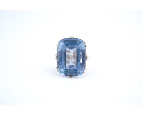 A blue topaz and 585 standard yellow metal cocktail ring, the cushion shaped stone (17 mm x 14 mm) crown set on a scroll-shou