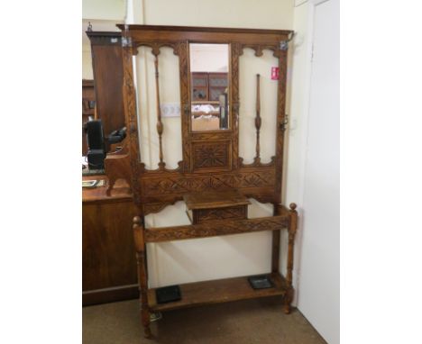 A solid, medium oak hall stand, with carved and turned detail, composed of bevelled mirror, hat and coat-hooks, glove box, tw