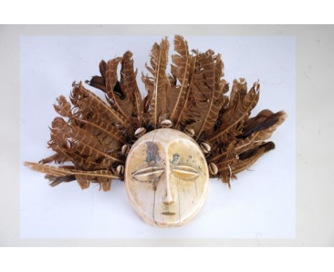 LEGA CARVED IVORY LUKUNGU MASK, with surround of cowrie shells and brown feathers, the mask, 4 ½" x 3 ¾" (11.4cm x 9.5cm)