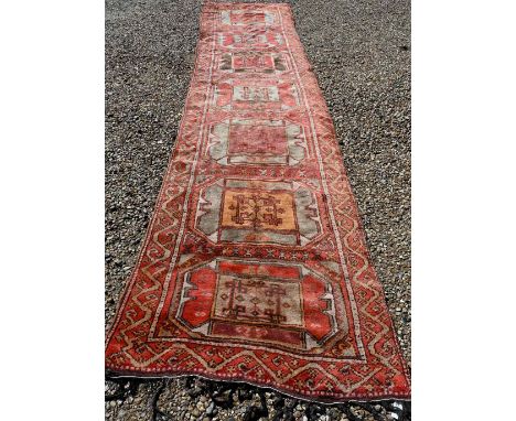 A vintage Kurdish red ground runner with seven octagonal medallions, 440 x 93 cm (extreme woof/curve) 