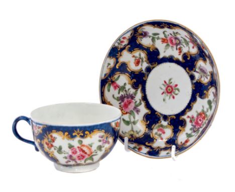 18th century Worcester tea cup and saucer with polychrome painted floral sprays and sprigs in gilt cartouches on blue scale g