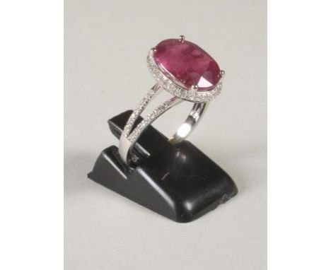 A RUBY AND DIAMOND RING, the oval cut ruby of approximately 5.30cts claw set to a border of pave set small diamonds to pave s