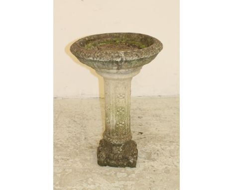 A COMPOSITION STONE BIRD BATH, the circular basin with moulded edge, raised on slender faceted leaf moulded stem, on square b