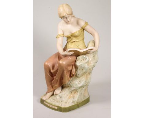 A ROYAL DUX PORCELAIN FIGURE, c.1900, of a young maiden wearing a draped top and skirt, reading a book and seated on a hilloc