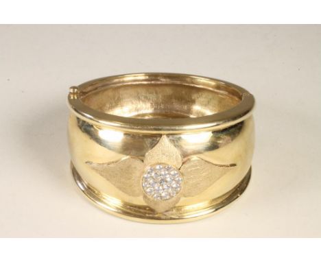 A 9CT GOLD STIFF HINGED BANGLE, the wide convex upper section gypsy set with a roundel of nineteen cubic zirconias to four ap