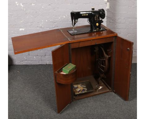 A Singer treadle sewing matching in walnut cabinet, with sewing lamp and other accessories.  