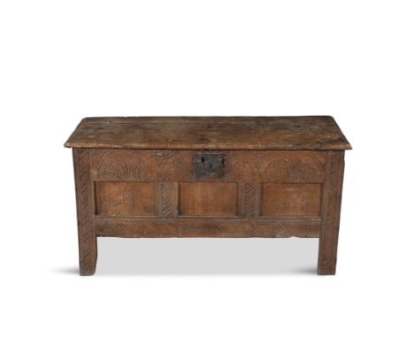 A 17TH CENTURY COMPACT CARVED OAK CHEST, the rectangular hinged lid above a carved three field panel front, raised on short s