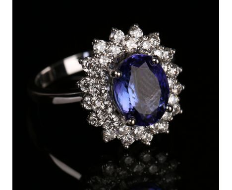 A white gold, tanzanite and diamond oval cluster ring, claw set with the oval cut tanzanite within a two row surround of circ