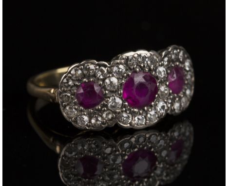 A gold, ruby and diamond triple cluster ring, mounted with three cushion shaped rubies, each in a surround of smaller cushion