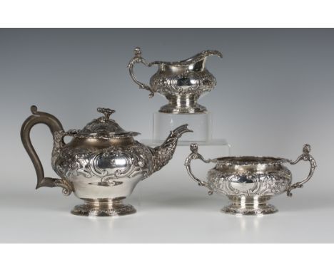 An Edwardian silver three piece tea set of circular form, relief decorated with 'C' scrolls, flowers and leaves, raised on a 