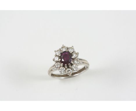 A RUBY AND DIAMOND CLUSTER RING the oval-shaped ruby is set within a surround of circular-cut diamonds, in 18ct. white gold. 