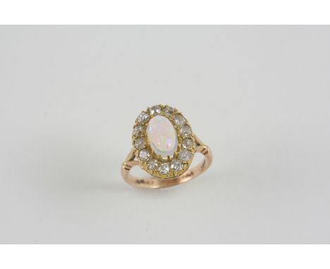 AN OPAL AND DIAMOND CLUSTER RING the oval solid white opal is set within a surround of old-cut diamonds, in 18ct. gold. Size 