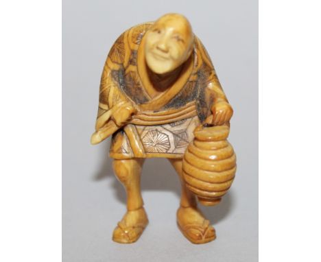 AN EARLY 20TH CENTURY SIGNED JAPANESE STAINED IVORY NETSUKE OF A NIGHT WATCHMAN, standing with hunched shoulders and bearing 