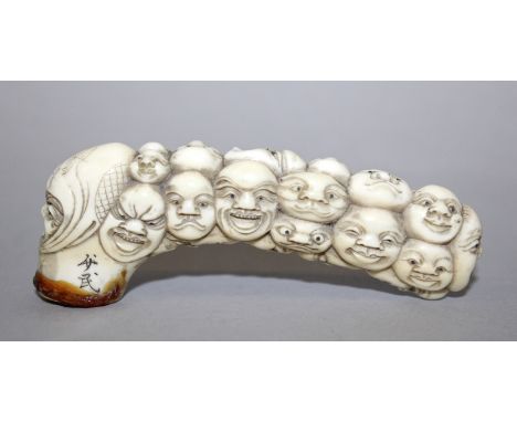 A GOOD QUALITY JAPANESE MEIJI PERIOD IVORY CANE HANDLE BY SYOUMIN, carved with a profusion of overlapping masks, 4in long.