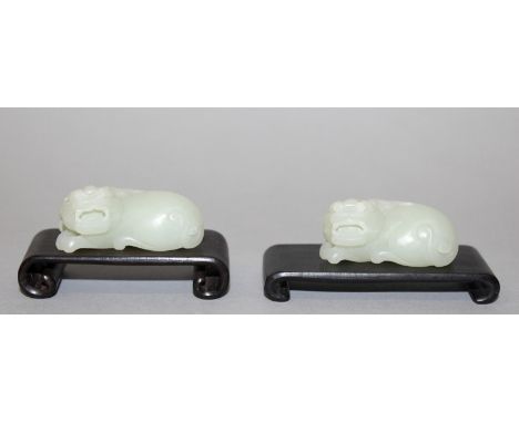 A SMALL PAIR OF CHINESE CELADON JADE-LIKE MODELS OF BUDDHISTIC LIONS, each with a scroll-end wood stand, the models themselve