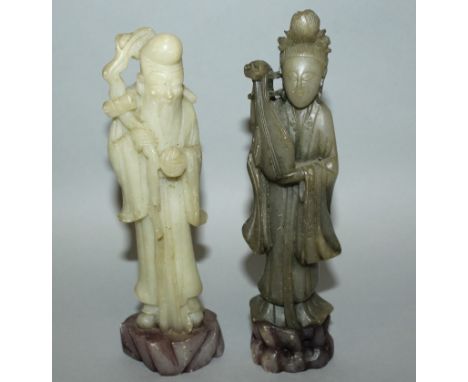 TWO 20TH CENTURY CHINESE CARVED SOAPSTONE IMMORTALS, each with a jade-like finish, each standing on a pierced rockwork plinth