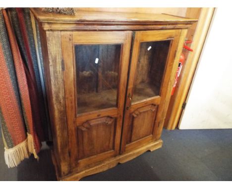 A rustic pine cabinet fitted with a pair of glazed panel doors enclosing a single shelf raised on plinth base 