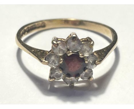 A 9 CARAT GOLD RING WITH A CENTRE RED STONE SURROUNDED BY EIGHT CLEAR STONES IN A FLOWER DESIGN SIZE K/L GROSS WEIGHT 1.33 GR