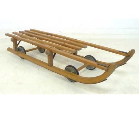 A vintage wooden 'Davos Flyer' sledge, labelled 'produced by Grays of Cambridge', with wheels as well as metal skids, 102 by 