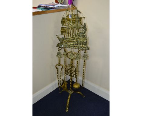 AN EARLY 20TH CENTURY BRASS FLOORSTANDING COMPANION SET, the frame cast with a ship on a barley twist support and tripod legs