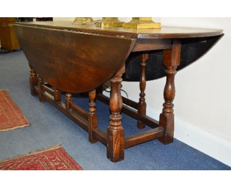 A REPRODUCTION GEORGIAN STYLE OAK WAKE TABLE, with two rounded drop leaves to form an oval supported by four pivoting gate le