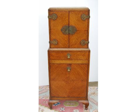 Edwardian oak cabinet on stand, the rectangular top above a cupboard with elaborate hinges and escutcheons, over frieze drawe