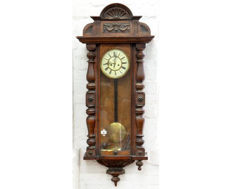 A CARVED WALNUT VIENNA WALL CLOCK WITH ENAMEL DIAL, EARLY 20TH C, 130cm h, 53CM W Chips and losses to veneer. Finials detache