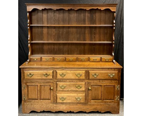 A George III style country kitchen oak dresser, shaped cornice, three tier plate rack top with seven small spice drawers to l